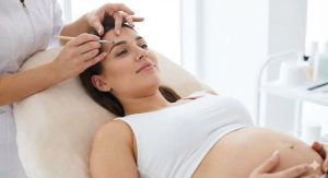 אישה מחייכת על מיטת טיפולים במהלך עיצוב גבות - חלק מפתרונות טיפוח להריוניות ומניקות.
